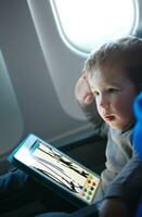 poco ragazzo disegno su un' tavoletta nel un aereo foto