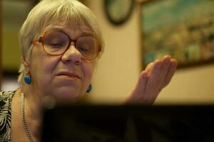 anziano donna Esprimere a gesti come lei legge su il computer portatile foto