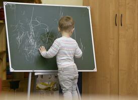 poco ragazzo disegno su un' lavagna a scuola materna foto