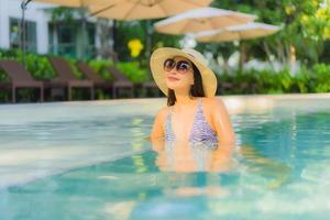 il sorriso felice delle belle giovani donne asiatiche si rilassa intorno alla piscina all'aperto nel resort dell'hotel per i viaggi in vacanza foto