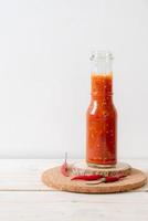 peperoncino o salsa di peperoncino in bottiglia e barattolo su fondo di legno foto