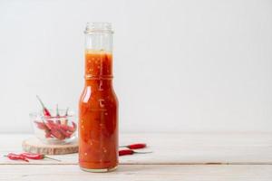 peperoncino o salsa di peperoncino in bottiglia e barattolo su fondo di legno foto