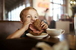 poco bambino avendo pranzo con Sandwich e tè nel bar foto