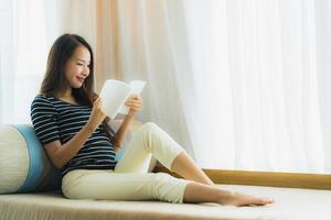 Ritratto di bella giovane donna asiatica che legge un libro sul divano nell'area soggiorno living