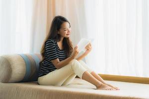 Ritratto di bella giovane donna asiatica che legge un libro sul divano nell'area soggiorno living