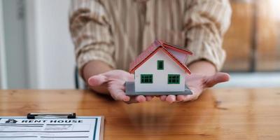 mani femminili che salvano la piccola casa con un tetto - architettura, sicurezza, protezione, immobiliare e concetto di proprietà - primo piano delle mani che proteggono la casa o il modello di casa foto