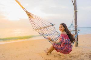 ritratto bella giovane donna asiatica seduta sull'amaca con sorriso felice spiaggia vicina mare e oceano foto