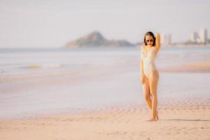 ritratto giovane bella donna asiatica camminare sorriso felice sulla spiaggia mare oceano con occhiali da sole foto