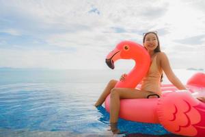 Ritratto di giovane donna asiatica sul fenicottero galleggiante gonfiabile intorno alla piscina all'aperto in hotel resort foto