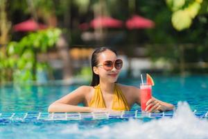 ritratto bella giovane donna asiatica tempo libero relax sorriso con succo di anguria intorno alla piscina in hotel resort foto