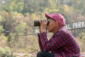 asiatico ragazzi detiene binocolo e Locale nazionale parco carta geografica, riposo e lettura informazione nel carta geografica vicino fionda ponte di Locale nazionale parco durante natura e estate campo di loro, adolescenti' attività concetto. foto