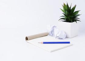 blocco note con matita blu e palla di carta e vaso di fiori su sfondo bianco foto