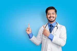 medico che indossa l'uniforme sorridente mentre presenta e indica isolato su sfondo blu con spazio di copia foto