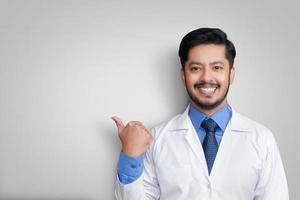 medico che indossa l'uniforme sorridente mentre presenta e indica isolato con spazio di copia foto