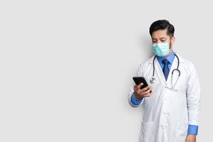 medico con maschera guardando il telefono. medico pakistano tecnologia medicina a casa spazio copia foto