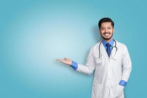 medico che indossa l'uniforme sorridente mentre presenta e indica isolato su sfondo blu con spazio di copia foto