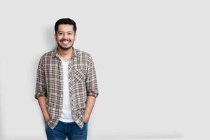 attraente bello uomo asiatico felice positivo. bel ragazzo pakistano asiatico che indossa una camicia a quadri marrone con un grande sorriso isolato su sfondo bianco foto