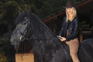 una bella ragazza bionda su un cavallo nero foto
