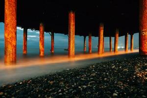 onde schiuma sotto il ponte, ferro colonne a il spiaggia. foto di onde su un' lungo esposizione. sera foto di il mare e colonne con ruggine