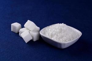 zollette di zucchero con zucchero in piatto bianco su sfondo blu foto