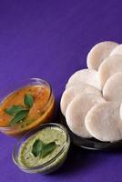 idli con sambar e chutney di cocco su sfondo viola, piatto indiano cibo preferito dell'India meridionale rava idli o semolino pigramente o rava pigramente, servito con sambar e chutney verde. foto