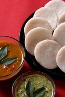 idli con sambar e chutney di cocco su sfondo rosso, piatto indiano cibo preferito dell'India meridionale rava idli o semolino pigramente o rava pigramente, servito con sambar e chutney verde.