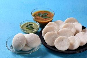 idli con sambar e chutney di cocco su sfondo blu, piatto indiano cibo preferito dell'India meridionale rava idli o semolino pigramente o rava pigramente, servito con sambar e chutney di cocco verde. foto