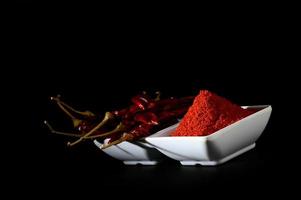 polvere fredda con peperoncino rosso in piatto bianco, peperoncini secchi su sfondo nero foto