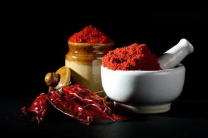 Peperoncino rosso in polvere in pestello con mortaio e vaso di argilla con peperoncino rosso su sfondo nero