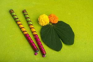 festival indiano dussehra e navratri, che mostra foglie d'oro bauhinia racemosa e fiori di calendula con bastoncini dandiya su sfondo verde foto