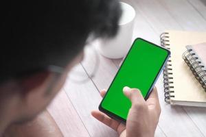 vista posteriore della mano del giovane che utilizza lo smartphone con lo schermo verde foto