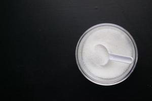 zucchero bianco e cucchiaio in un contenitore su sfondo nero, foto