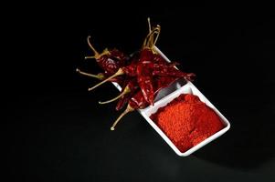 polvere fredda con peperoncino rosso in piatto bianco, peperoncini secchi su sfondo nero foto