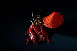 polvere fredda in una ciotola nera con peperoncino rosso, peperoncino secco su sfondo nero foto