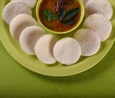 idli con sambar in una ciotola su sfondo verde, piatto indiano cibo preferito dell'India meridionale rava idli o semolino pigramente o rava pigramente, servito con sambar e chutney di cocco verde. foto