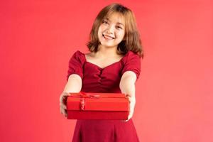 ragazza asiatica in abito con scatola regalo rossa con espressione allegra sullo sfondo