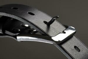 parte di un' nero pelle cintura con un' metallo fibbia avvicinamento su un' grigio sfondo. foto