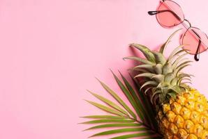 concetto estivo con ananas, occhiali da sole e foglia di palma su sfondo rosa pink foto