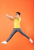 uomo asiatico in maglietta gialla che salta su sfondo arancione foto