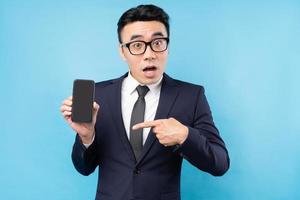 uomo d'affari asiatico che indossa tuta tenendo lo smartphone su sfondo blu foto