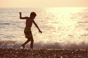 silhouette di un' ragazzo di il mare a tramonto. lui corre lungo il costa, giochi con il onda. foto