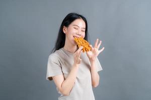 giovane donna asiatica che indossa un maglione con una faccia felice e si diverte a mangiare pollo fritto su sfondo grigio foto