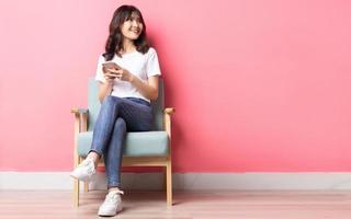 donna asiatica seduta sul divano usando il suo telefono con un'espressione felice
