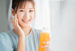 la giovane donna asiatica beve succo d'arancia accanto alla finestra al mattino? foto