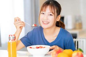 una giovane donna asiatica che fa colazione con la frutta nella sua cucina foto