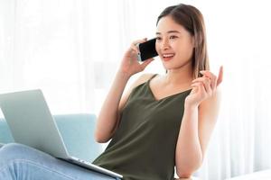 donna asiatica che parla al telefono mentre usa il laptop foto