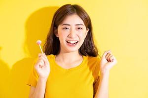 giovane donna asiatica che mangia lecca-lecca su sfondo giallo foto