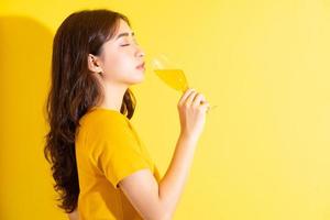 giovane donna asiatica che beve vino e posa su sfondo giallo
