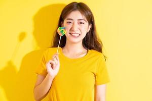 giovane donna asiatica che mangia lecca-lecca su sfondo giallo foto