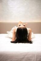 un asiatico donna con nero capelli è addormentato su un' bianca letto nel un elegante Hotel foto